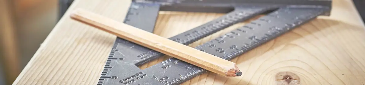 Anschlagwinkel und Zimmermannsbleistift auf einem Holzbrett in der Werkstatt