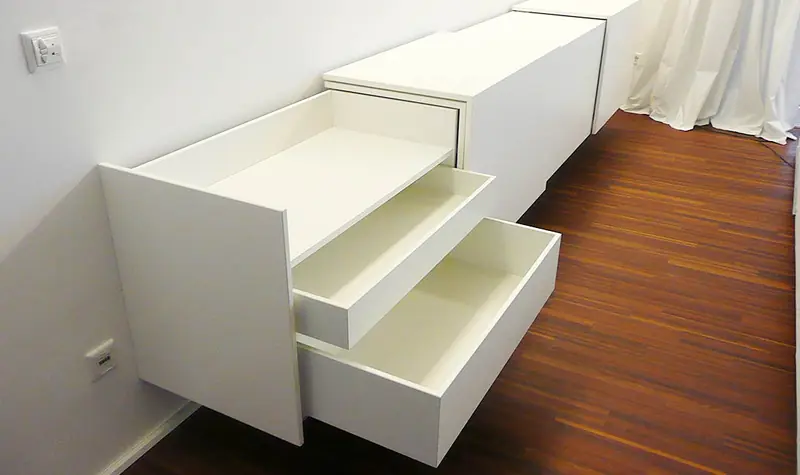 Weißes Einbaumöbel mit ausgezogenen Schubkästen vor einem Holzdielenboden